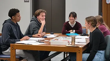 Five friends studying together at table in library.